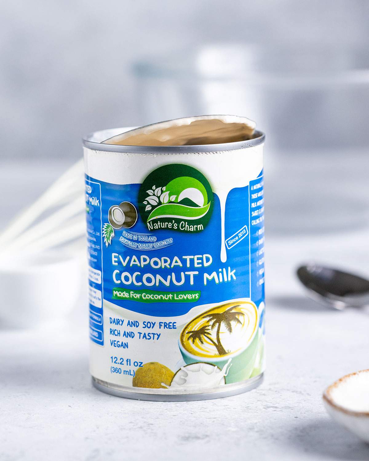 An opened can of Nature's Charm Evaporated Coconut Milk on a white table.