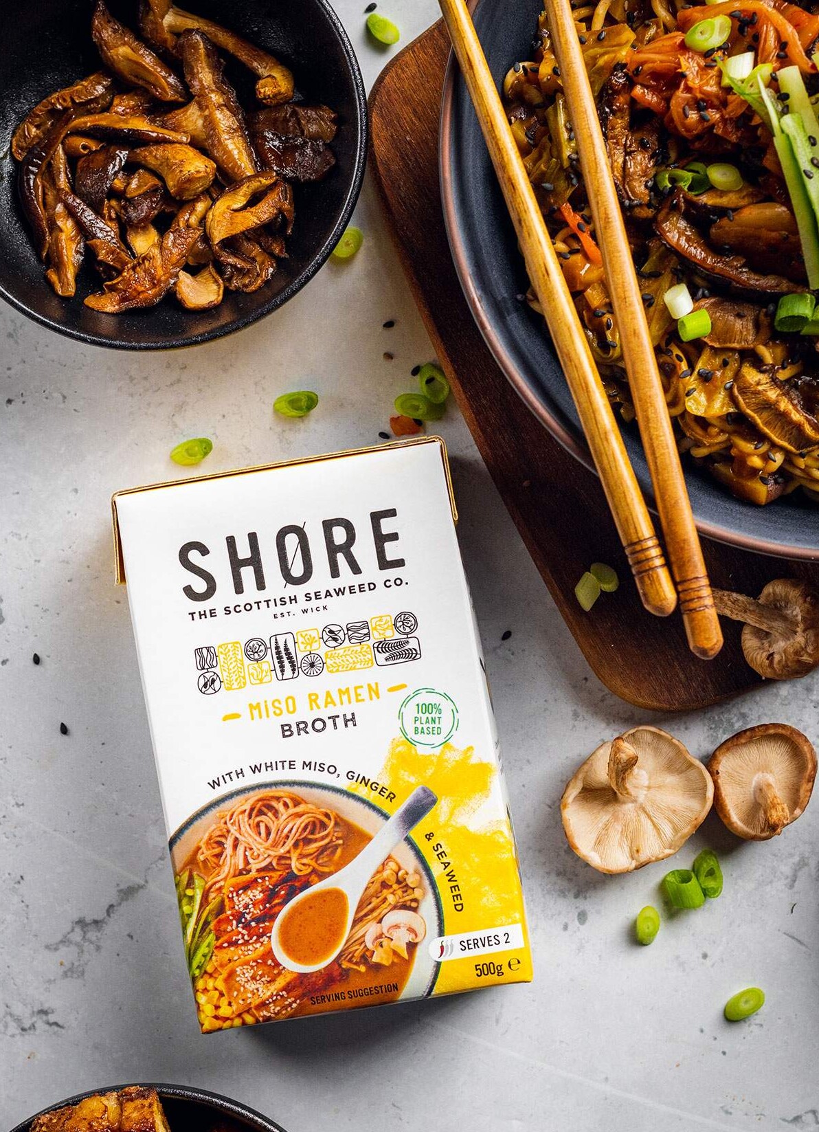 A pack of Shore Miso RAmen Broth on a white table next to a bowl of vegan ramen.