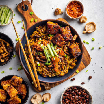 A bowl of vegan black bean ramen on a white table surrounded by ingredients.