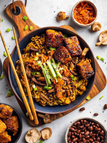 A bowl of vegan black bean ramen on a white table surrounded by ingredients.