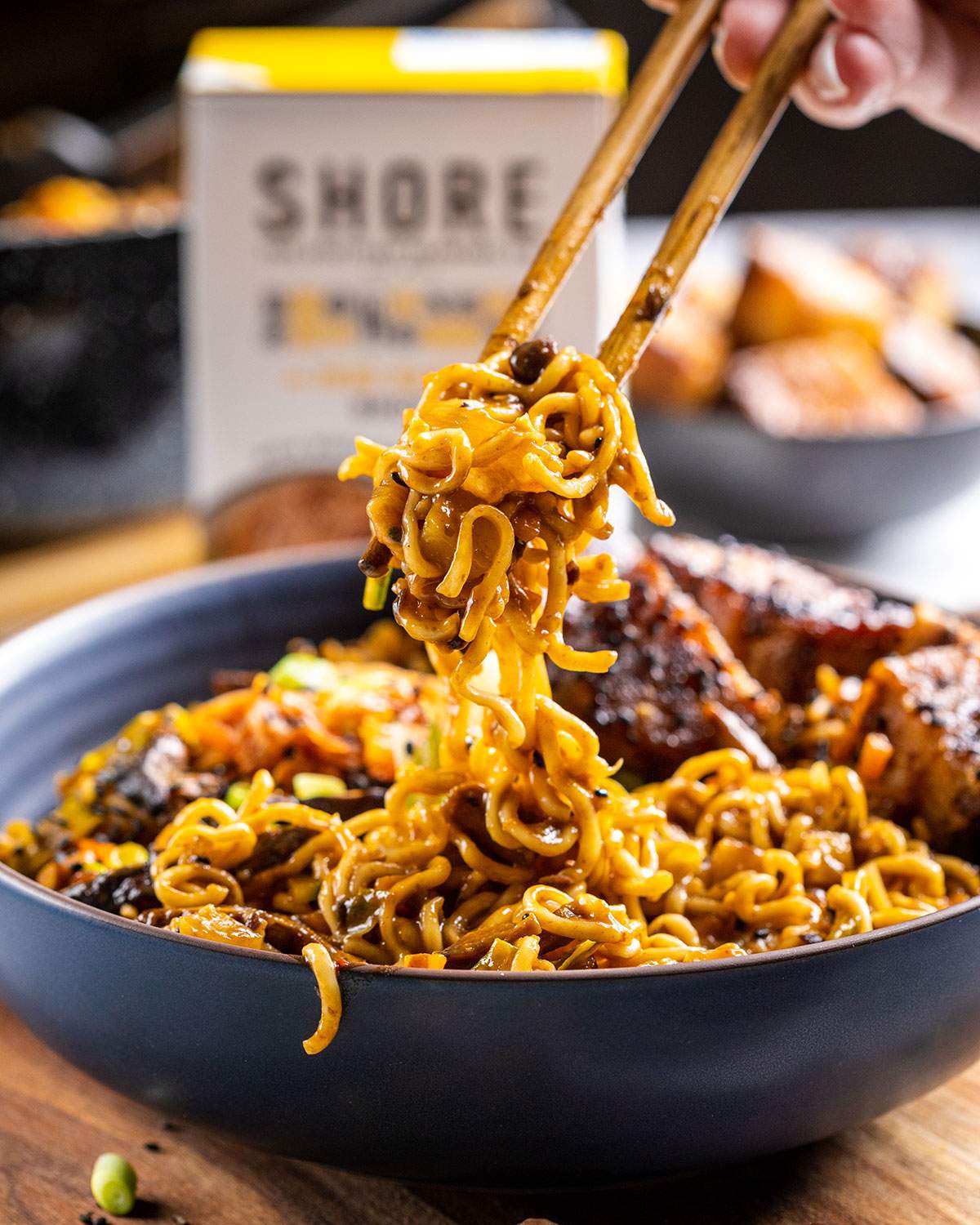 Chopsticks picking up plant-based black bean ramen noodles from a black bowl.