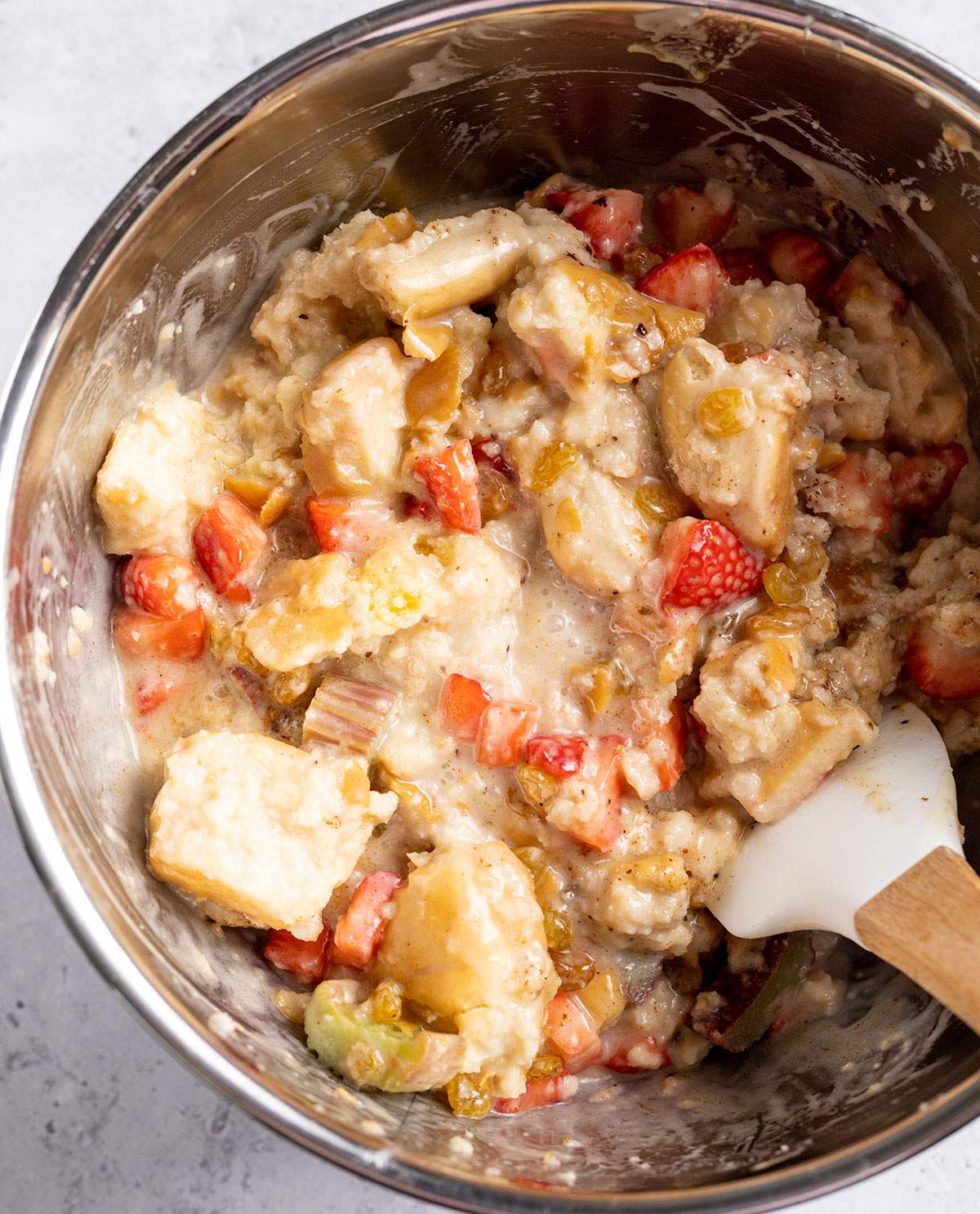 Mixed vegan bread pudding ingredients in a large bowl with a spatula on the side.