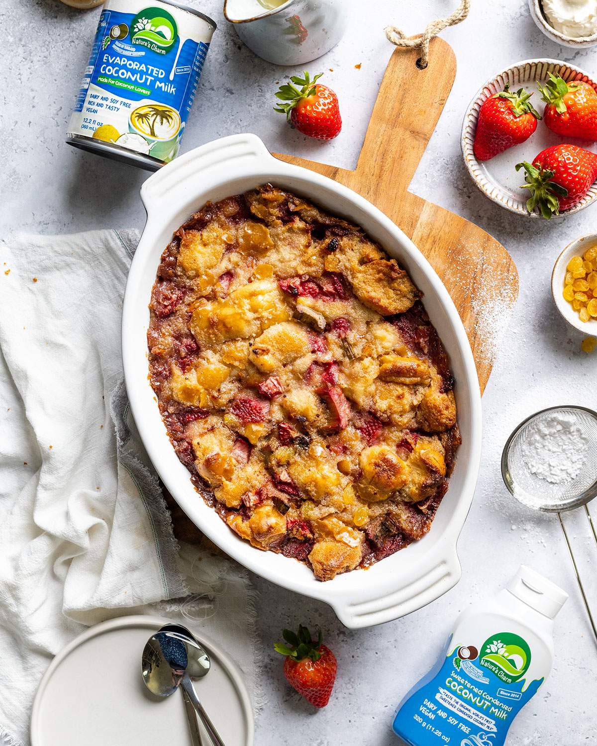 Vegan Bread Pudding after baking in a white oven dish sitting on a wooden serving board next to ingredients.