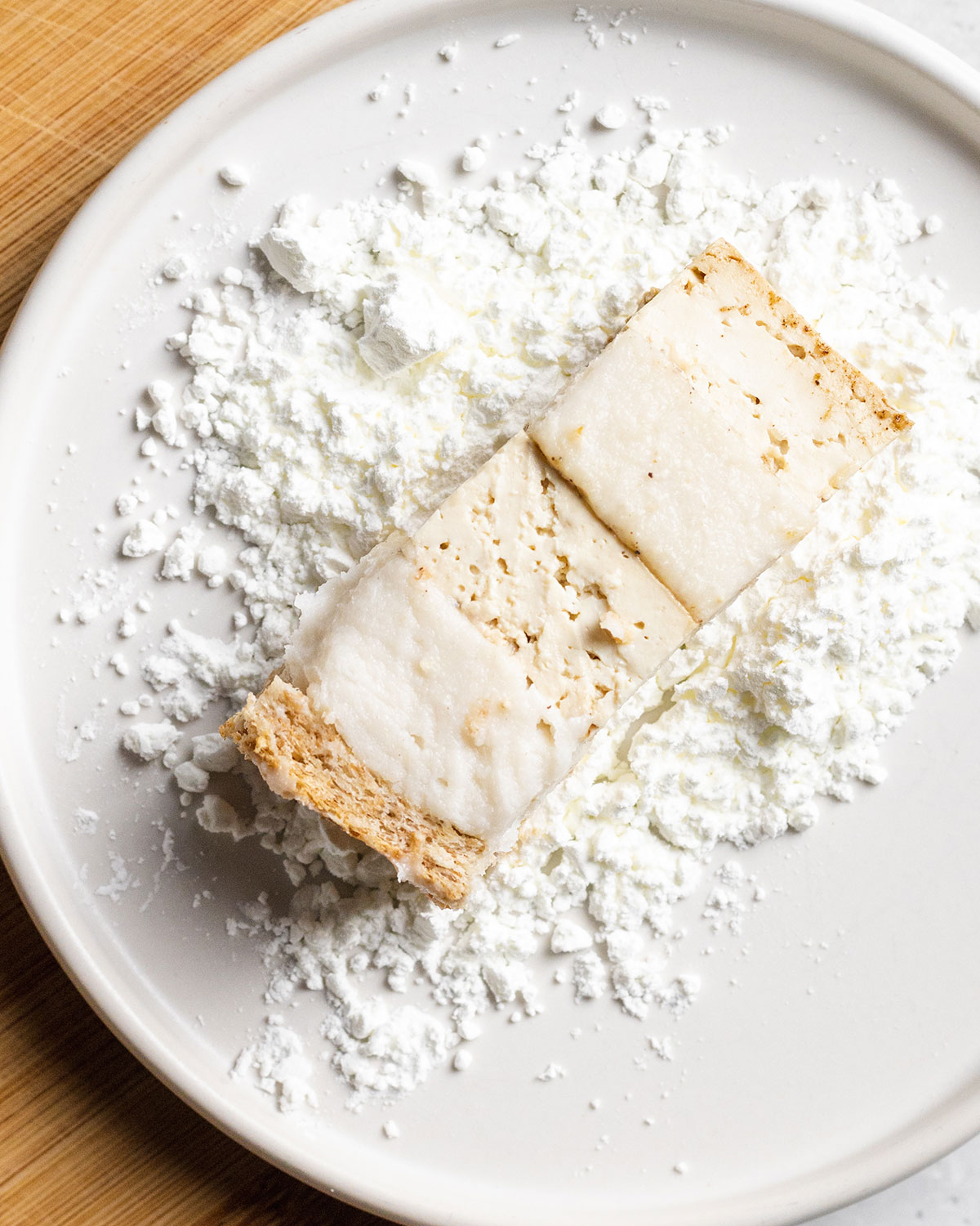 A piece of uncooked vegan pork belly on a plate with cornstarch.