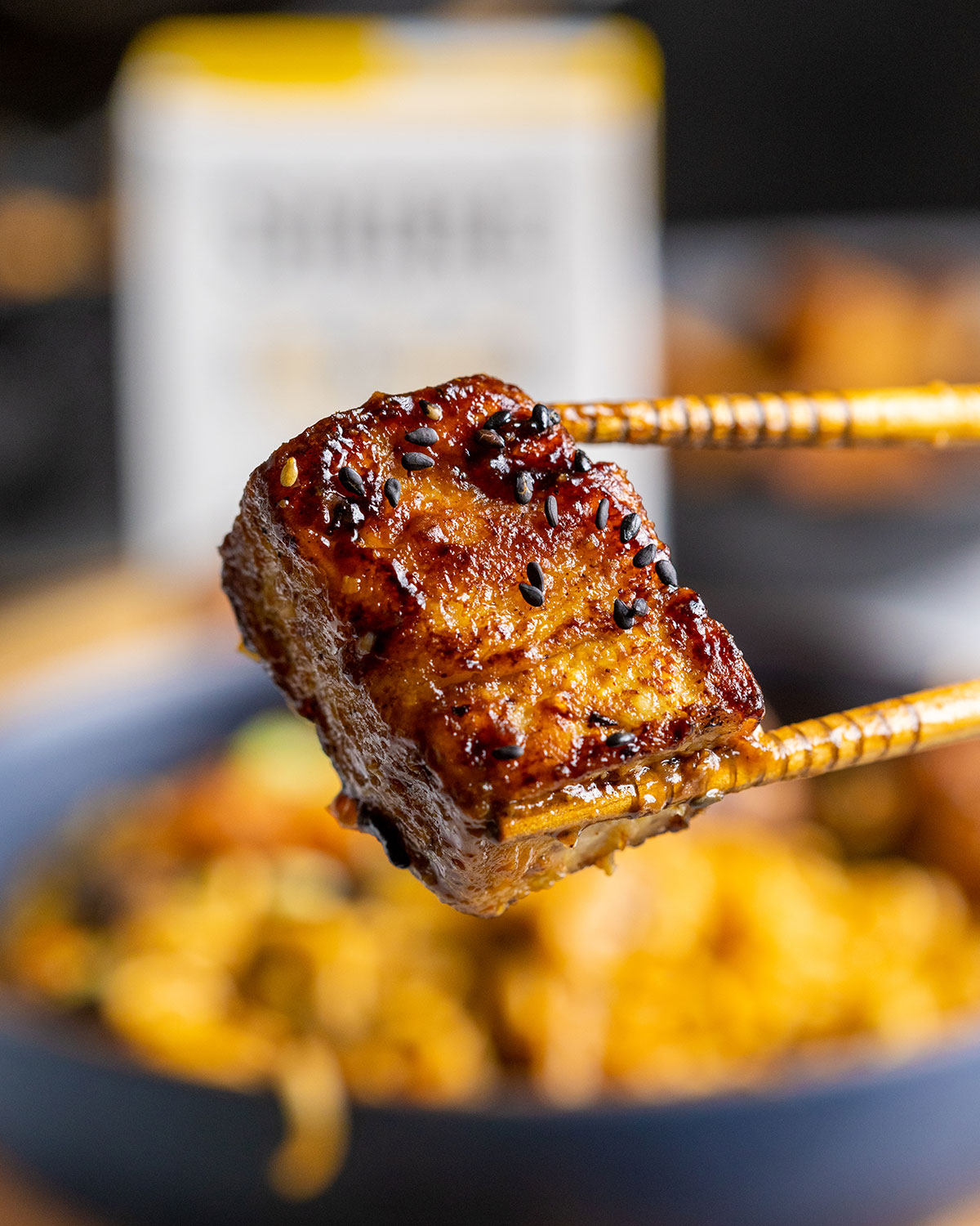 Wooden chopsticks holding a piece of vegan pork belly into the camera.