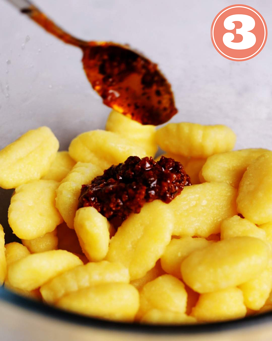 Vegan red pesto being added to a bowl of cooked gnocchi.