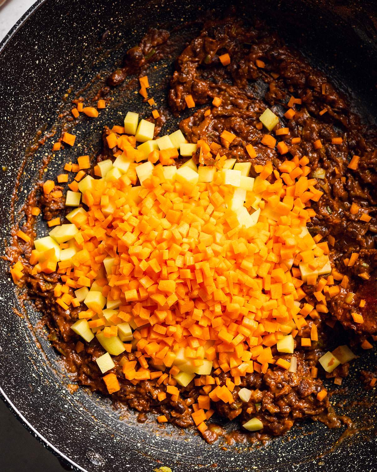 Finely diced carrots on top of black bean sauce in a wok.