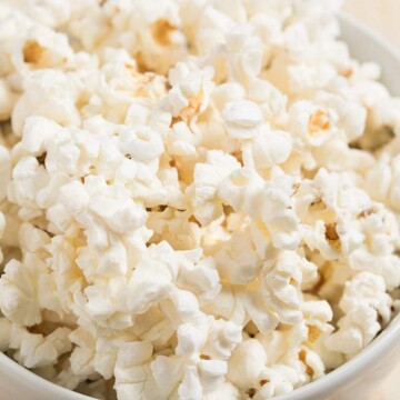 A white bowl filled with cooked popcorn on a light wooden table.