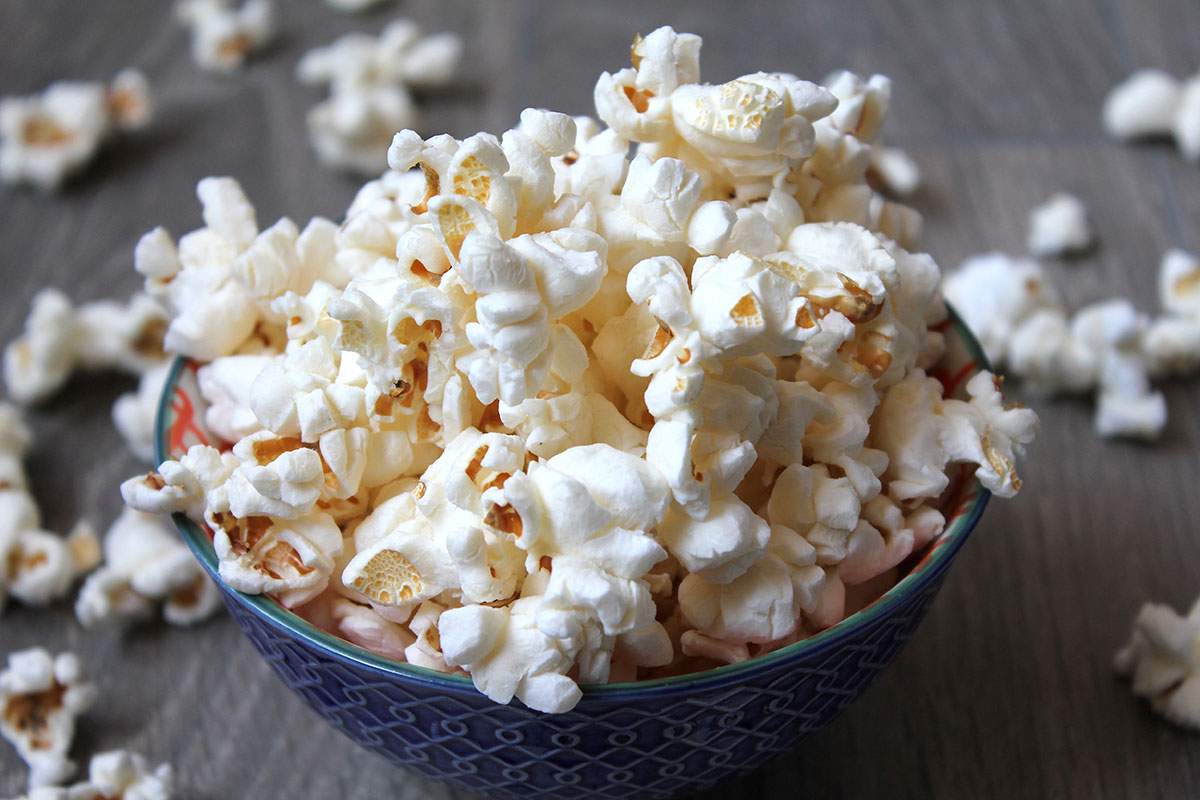 A small bowl of popped popcorn sitting on a wooden table.