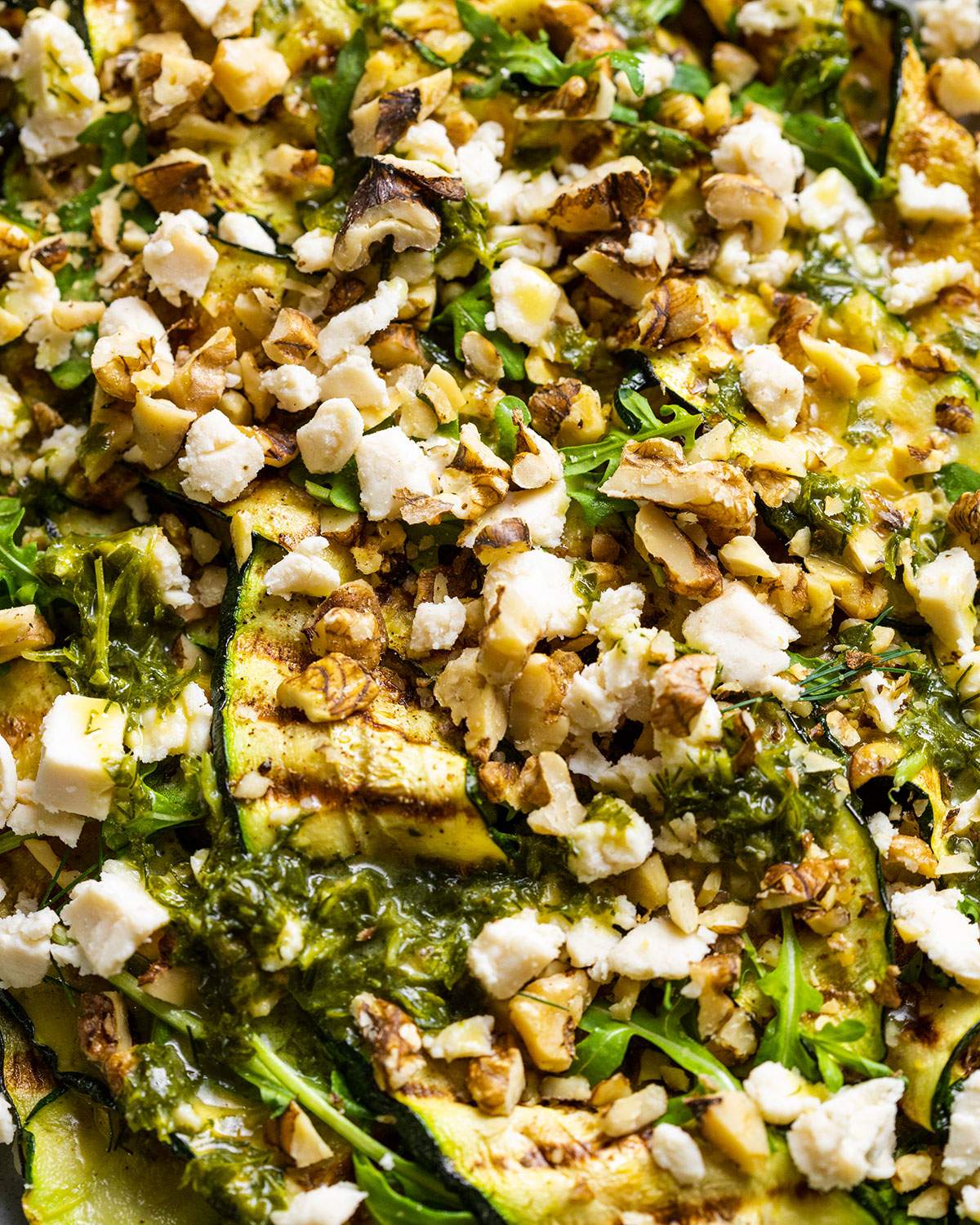 Vegan Grilled Zucchini Salad with walnuts and vegan feta crumbles on a serving platter, shown up close.