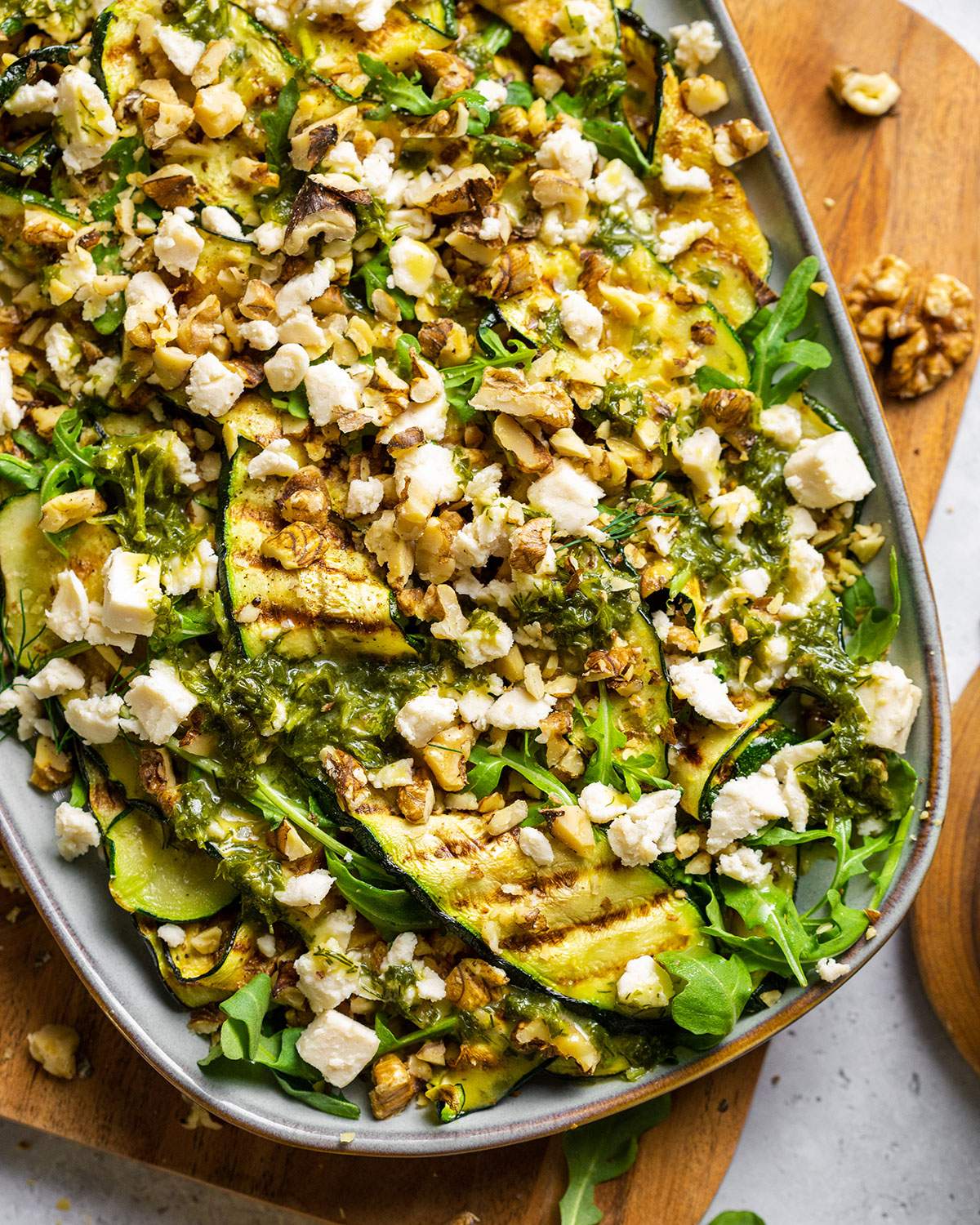 Vegan Grilled Zucchini Salad with walnuts and vegan feta crumbles on a serving platter, shown up close.