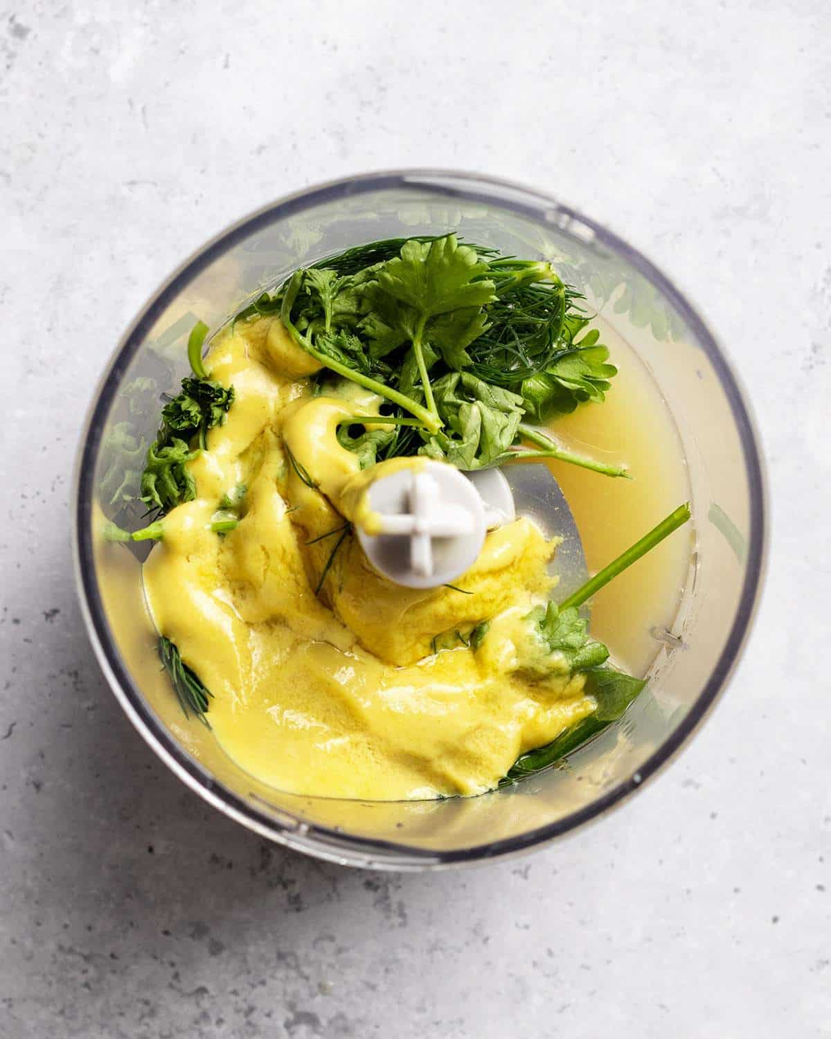 All ingredients for a simple oil free salad dressing are sitting together in a small blender bowl before blending. The fresh herbs, lemon juice and mustard can be seen clearly.