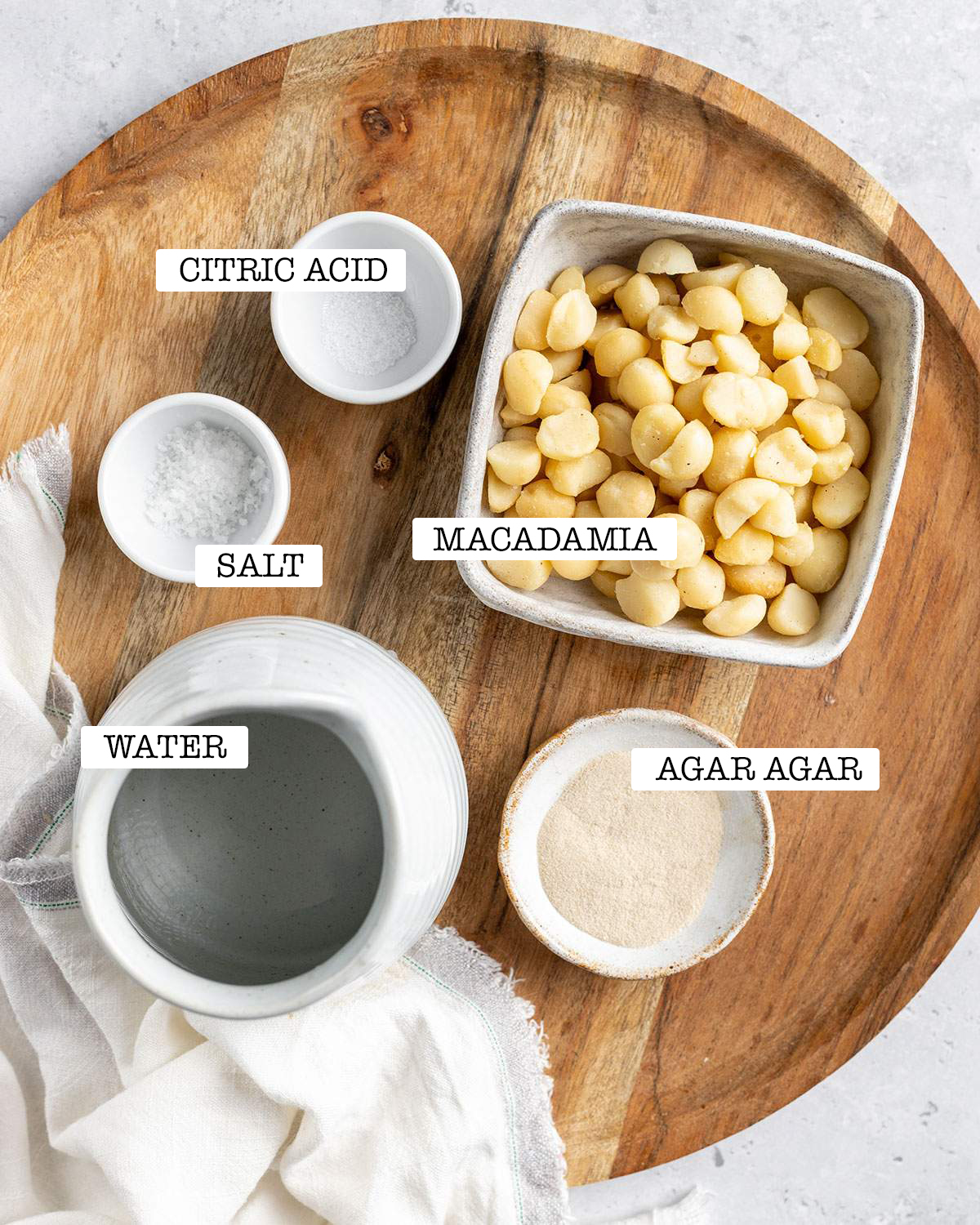 The ingredients for homemade vegan feta including macadamia nuts are sitting on a wooden tray with labels.