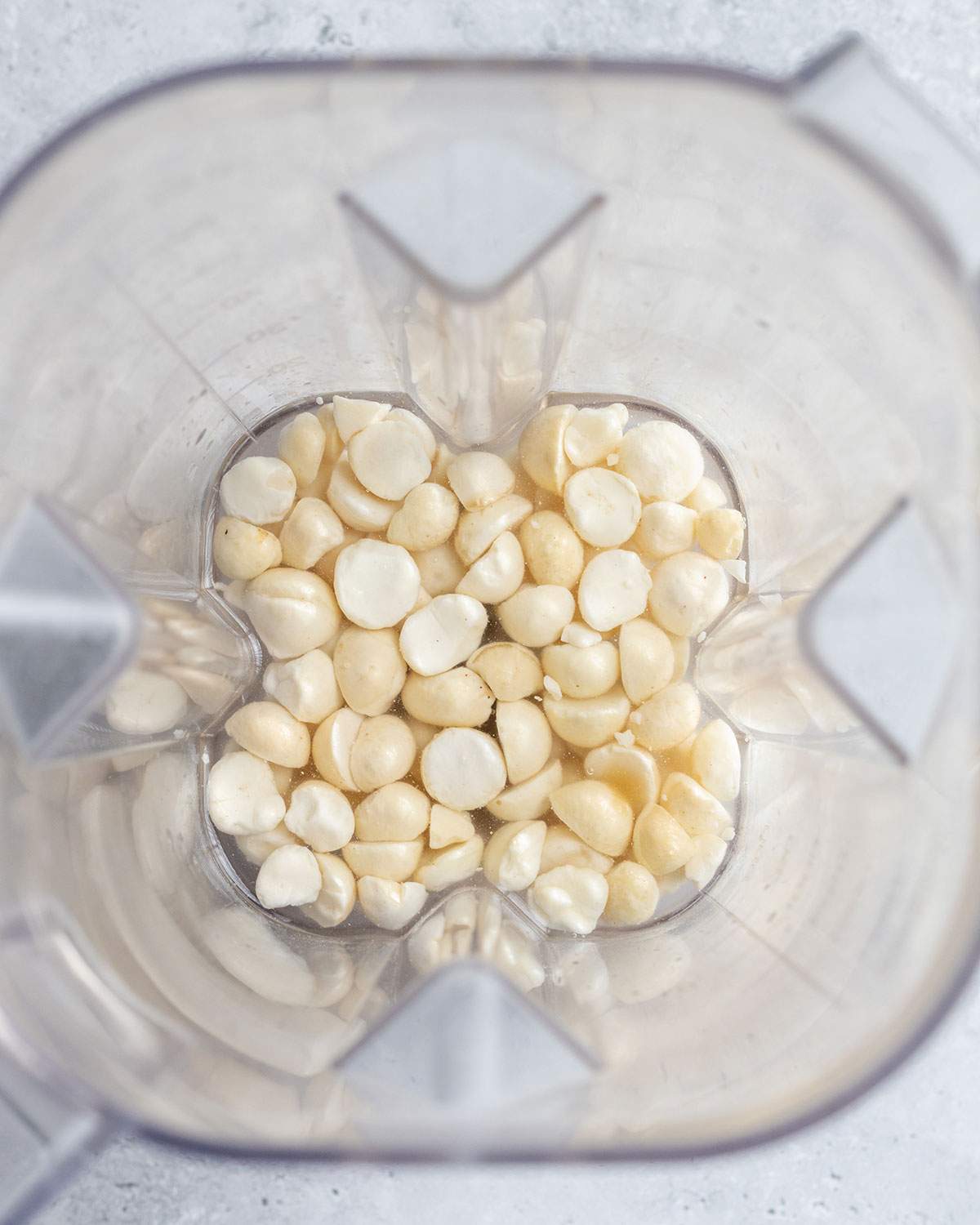 Soaked macadamia nuts in filtered water sitting at the bottom of a blender.
