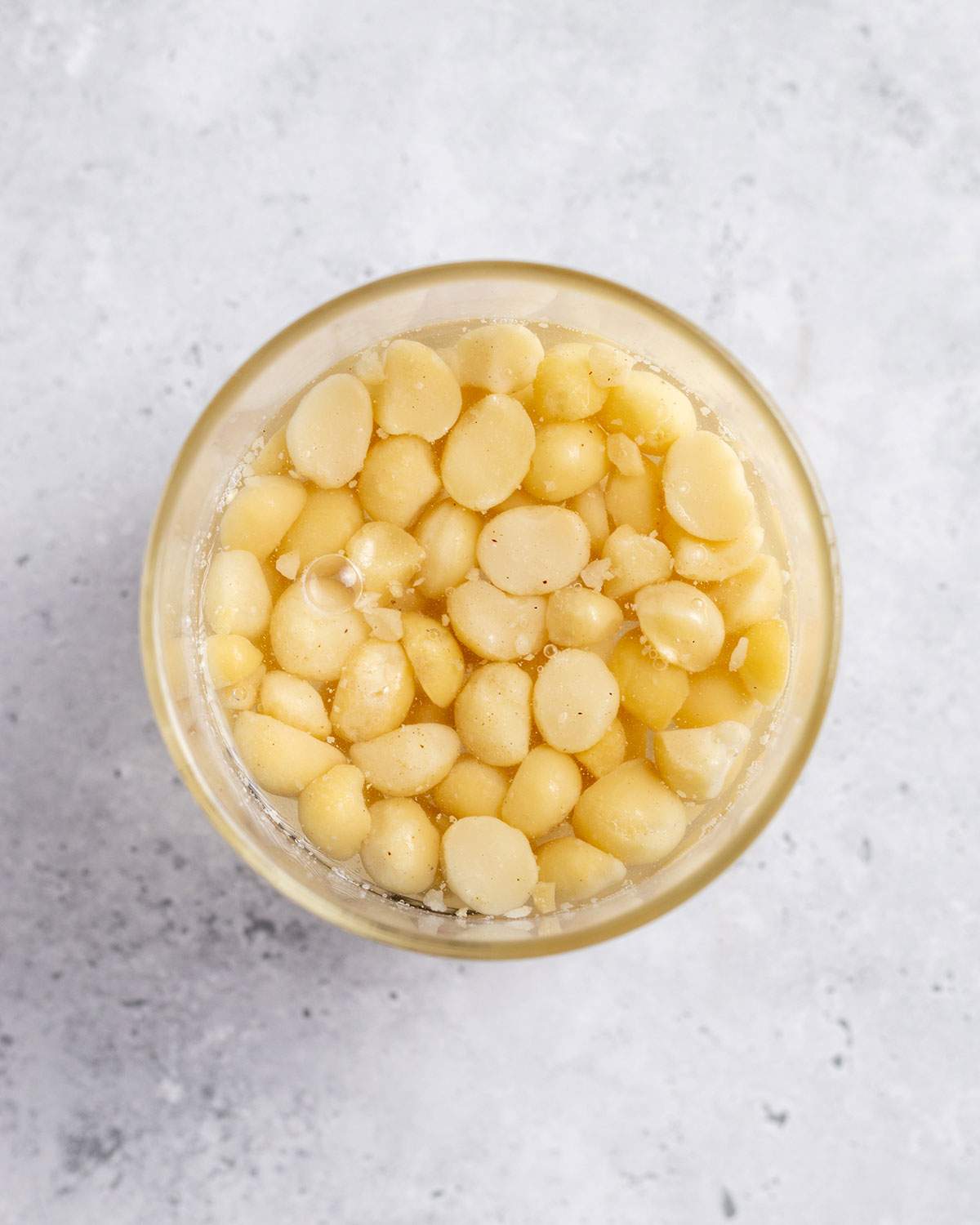 A handful of macadamia nuts are soaking in water in a glass jug.