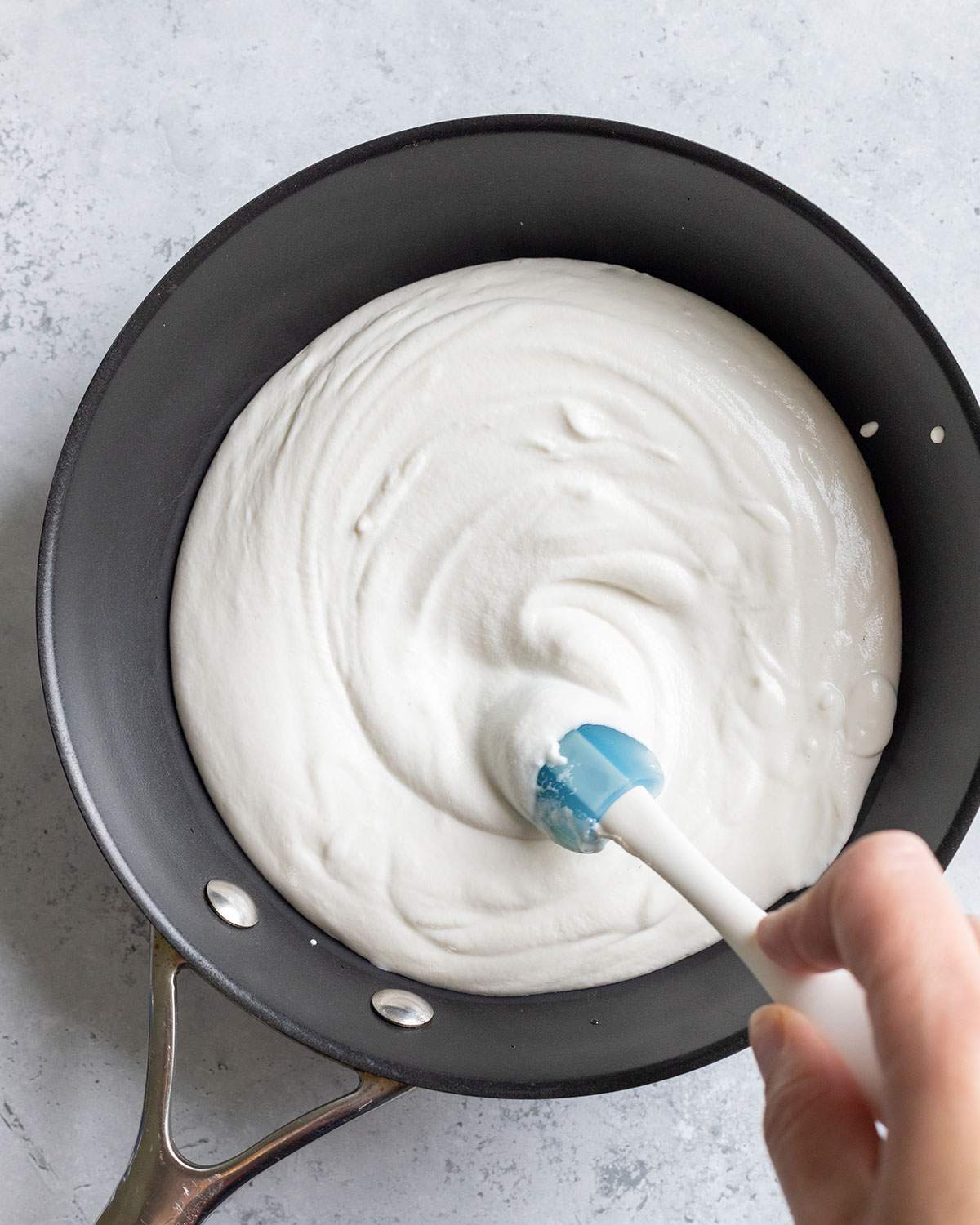 A spatula is stirring a vegan feta cheese mix in a black pan.