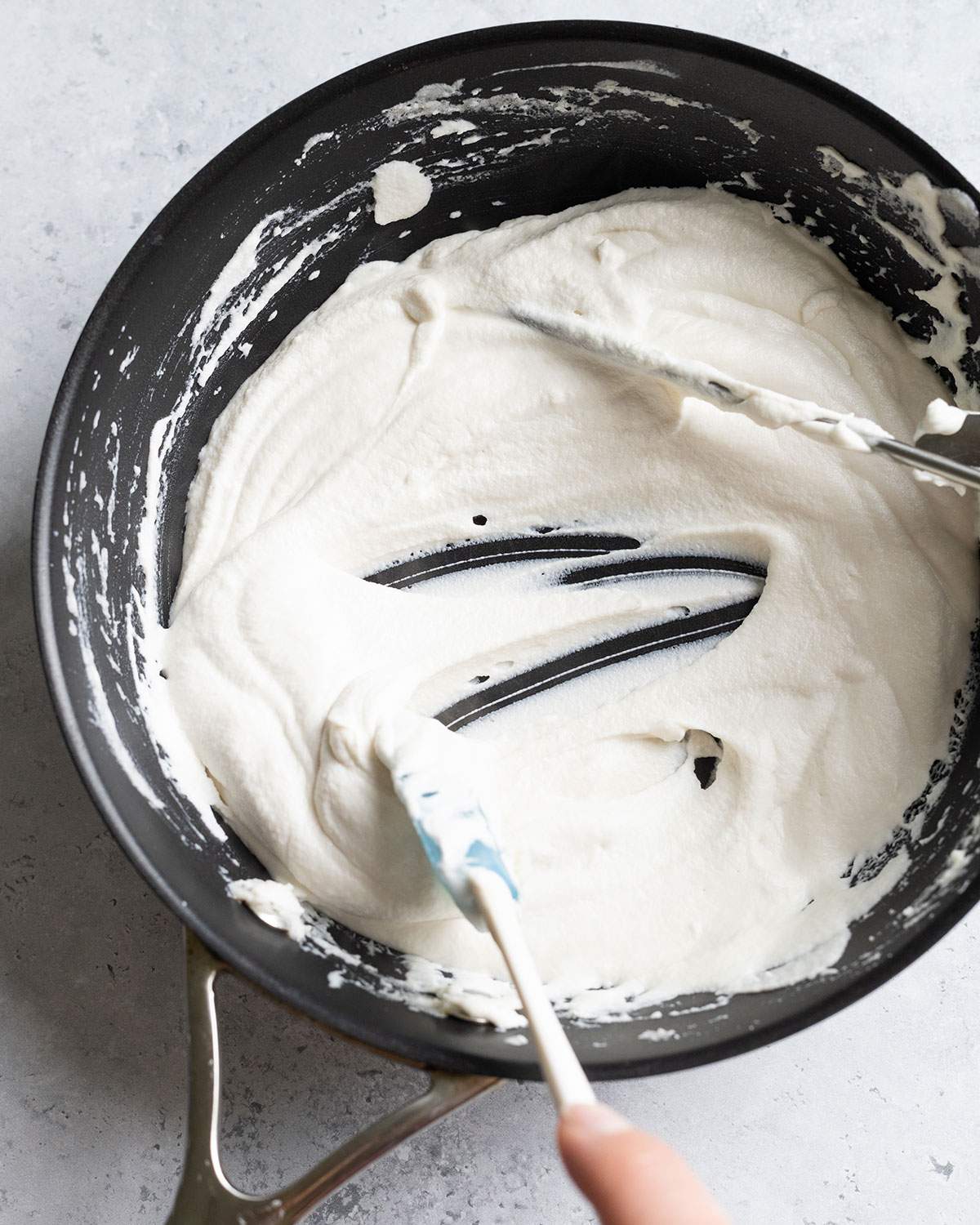 The cheese mix in the pan is thickening and a spatula swirling through it shows the firming texture.