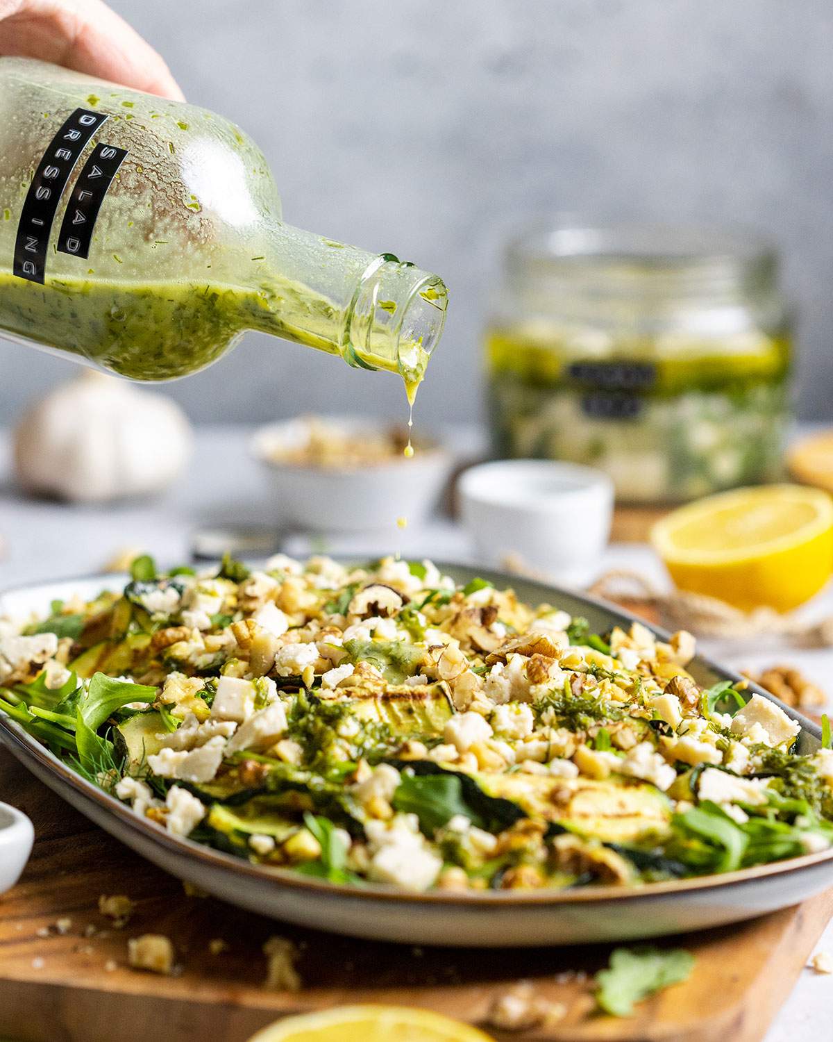 A hand is holding a glass bottle with oil-free salad dressing and drizzling the dressing onto a green salad.