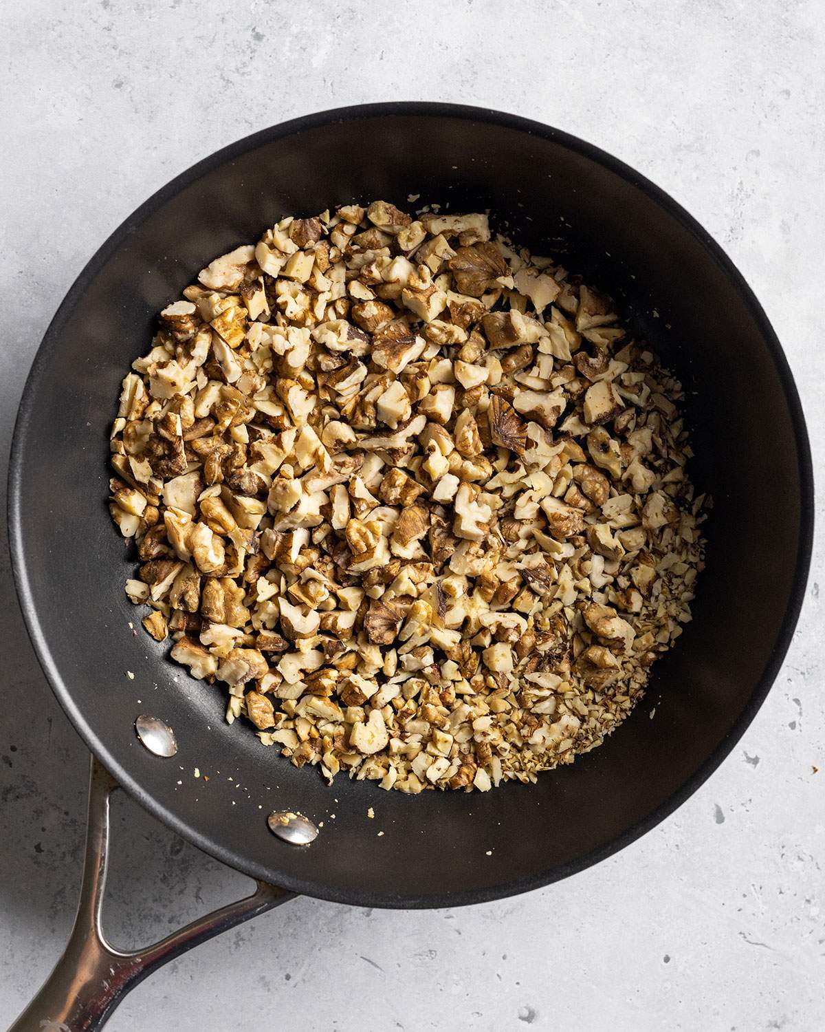 Walnuts have been chopped up and are toasting in a non-stick pan.