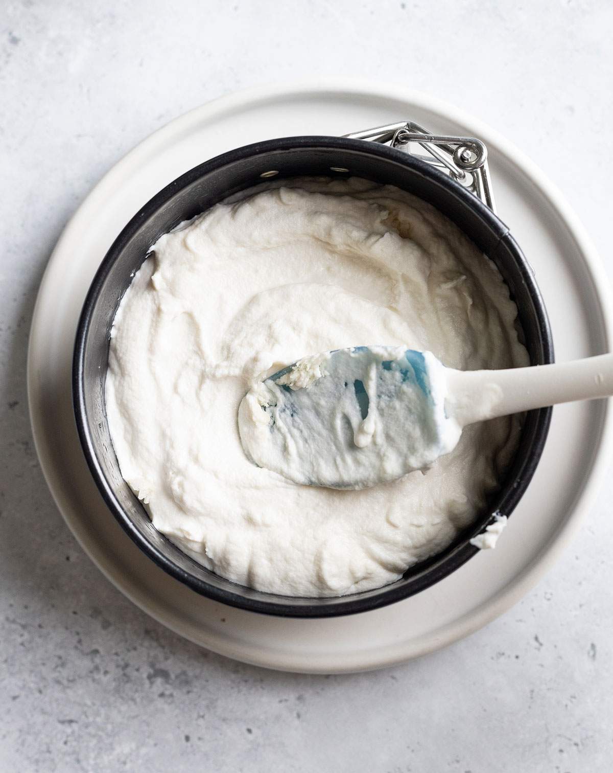 A spatula is spreading the vegan cheese mix into a round spring form pan.