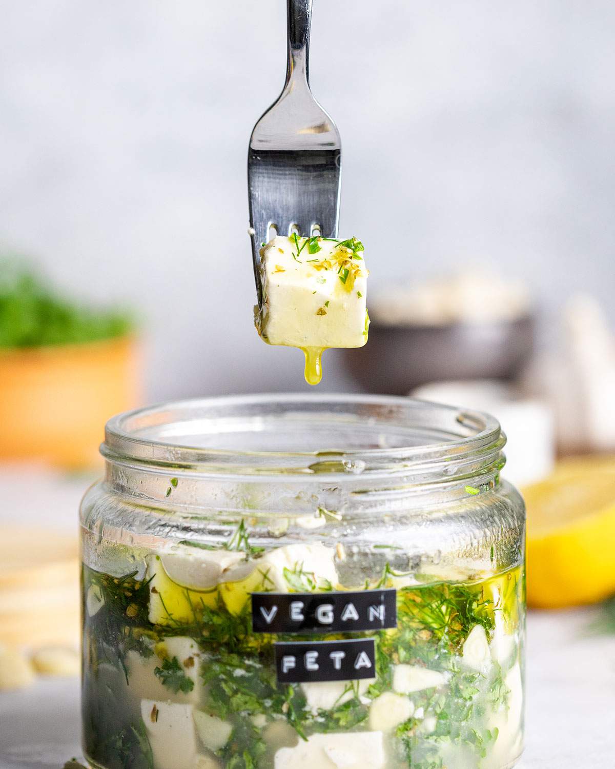 A fork is listing a cube of vegan feta out of a jar filled with more feta and marinade.