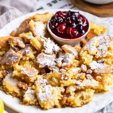 Fluffy vegan scrambled pancake is shown on a white plate with a bowl of stewed cherries on the side.