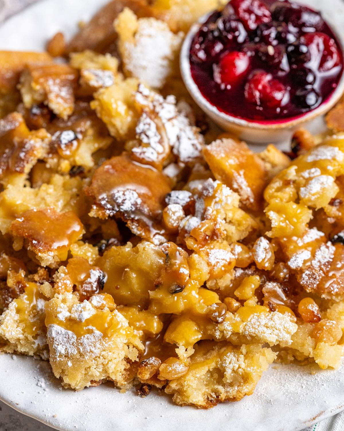 Torn pancakes are shown up close with a dusting of powered sugar and a drizzle of vegan salted caramel sauce over the top.