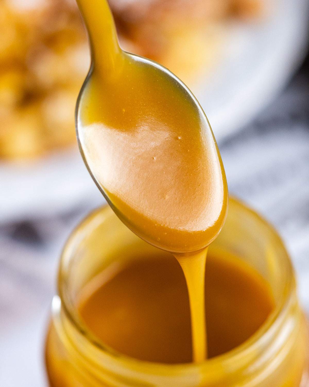 A spoon is lifting gooey caramel sauce out of an open jar.