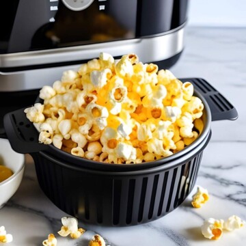 Popped popcorn kernels can be seen in a black air fryer basket on the kitchen counter with the air fryer standing behind.