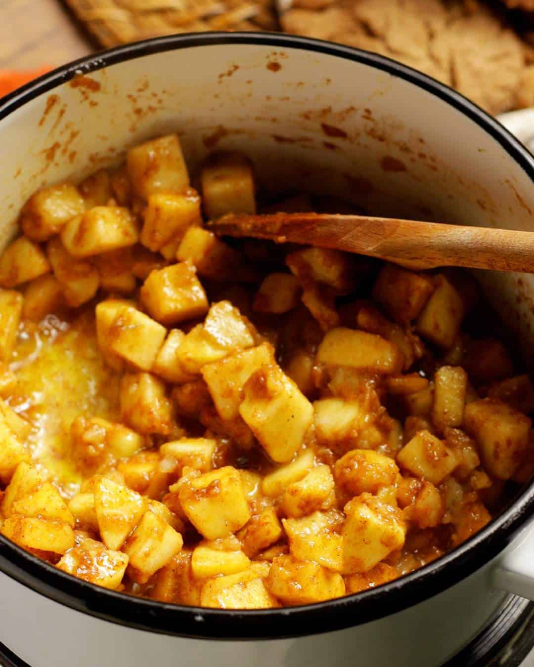 Caramelised apple cubes are being stirred in a saucepan. They are coated in warming spices.