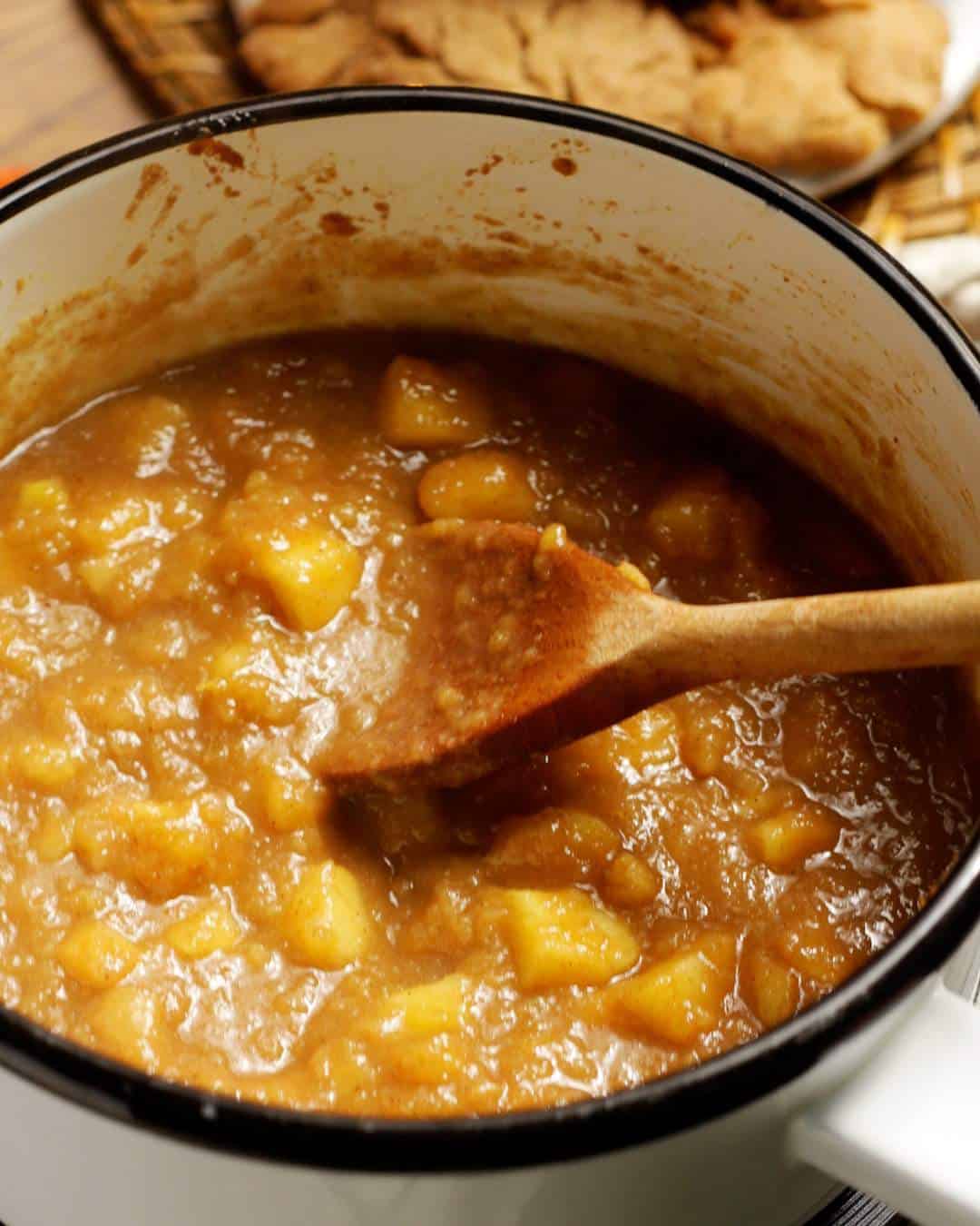 Caramelized apple mix can be seen in a saucepan with a wooden spoon.
