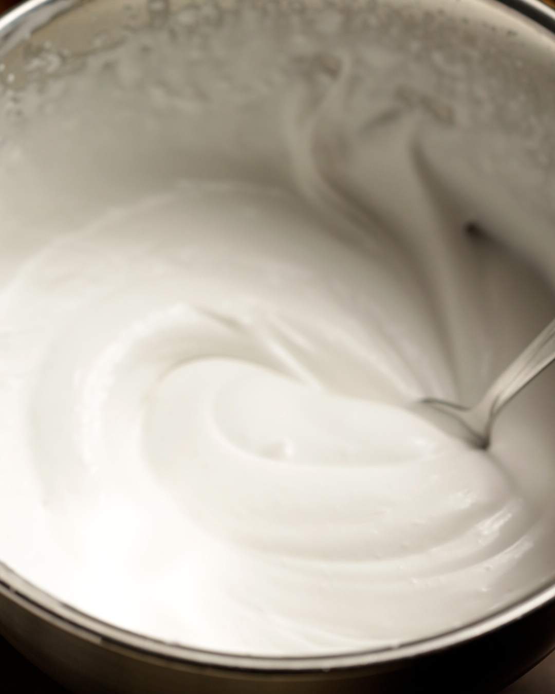 Spooning peaks of whipped coconut cream out of a mixing bowl.