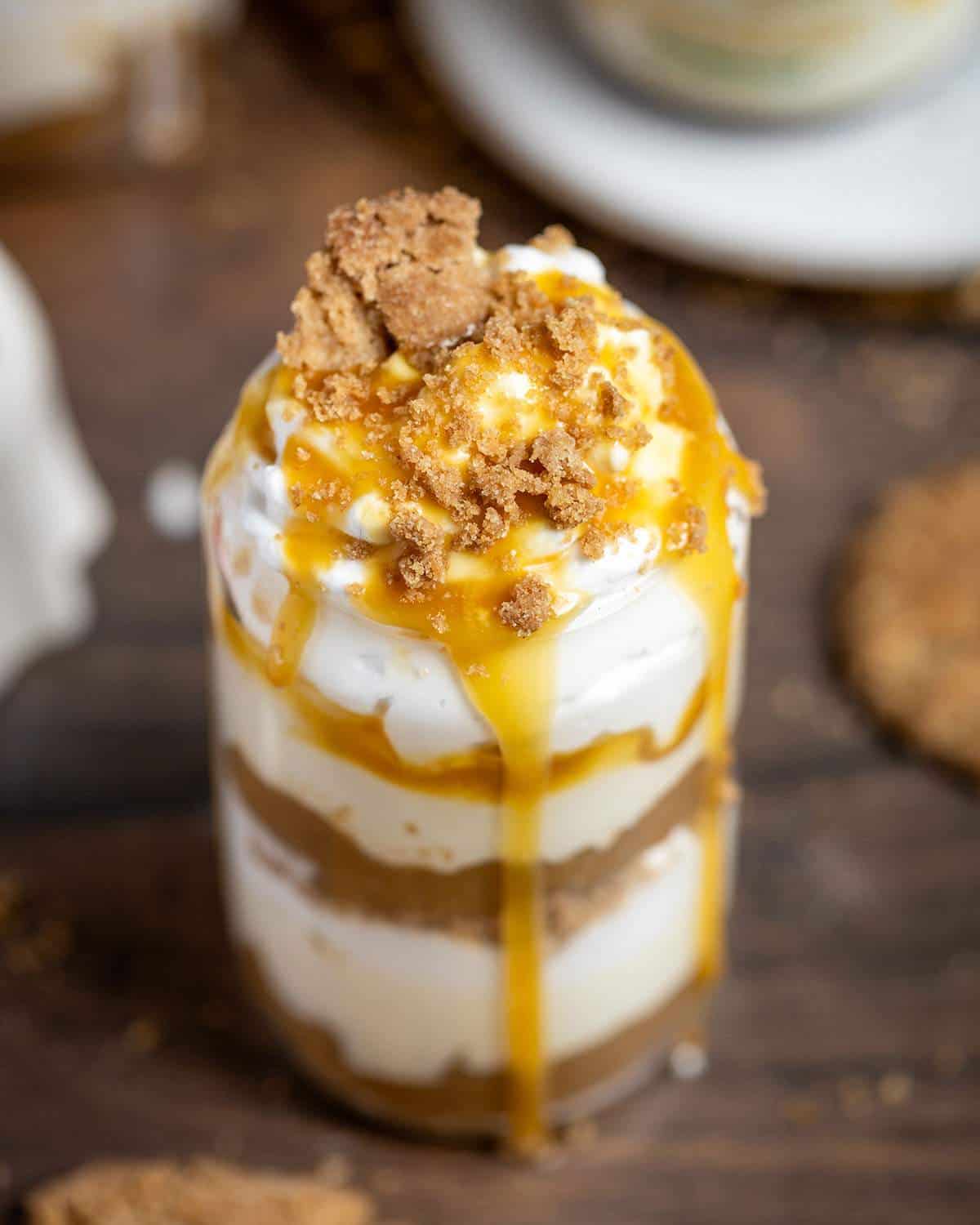 A portion of vegan apple parfait in a glass is shown up close with the focus on the cinnamon cookie crumbs on top of the parfait.