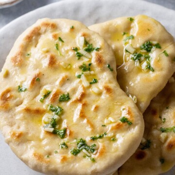 Three homemade vegan garlic naan breads are placed on a serving platter.