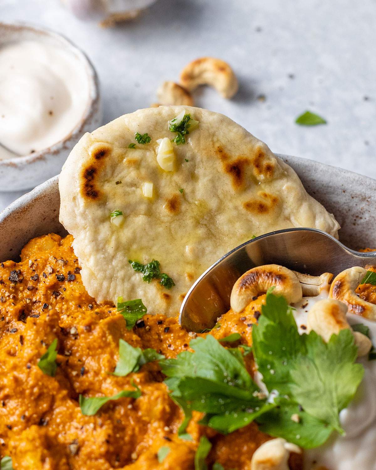 A homemade naan bread is sitting on a corner of a serving of vegan tikka masala curry. 