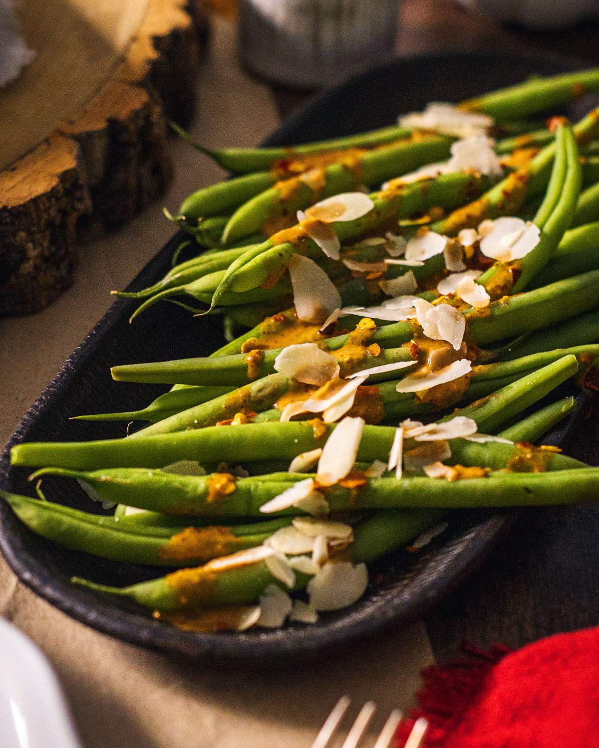 Cooked green beans on a serving platter drizzled with a spicy sauce and almond flakes on top.