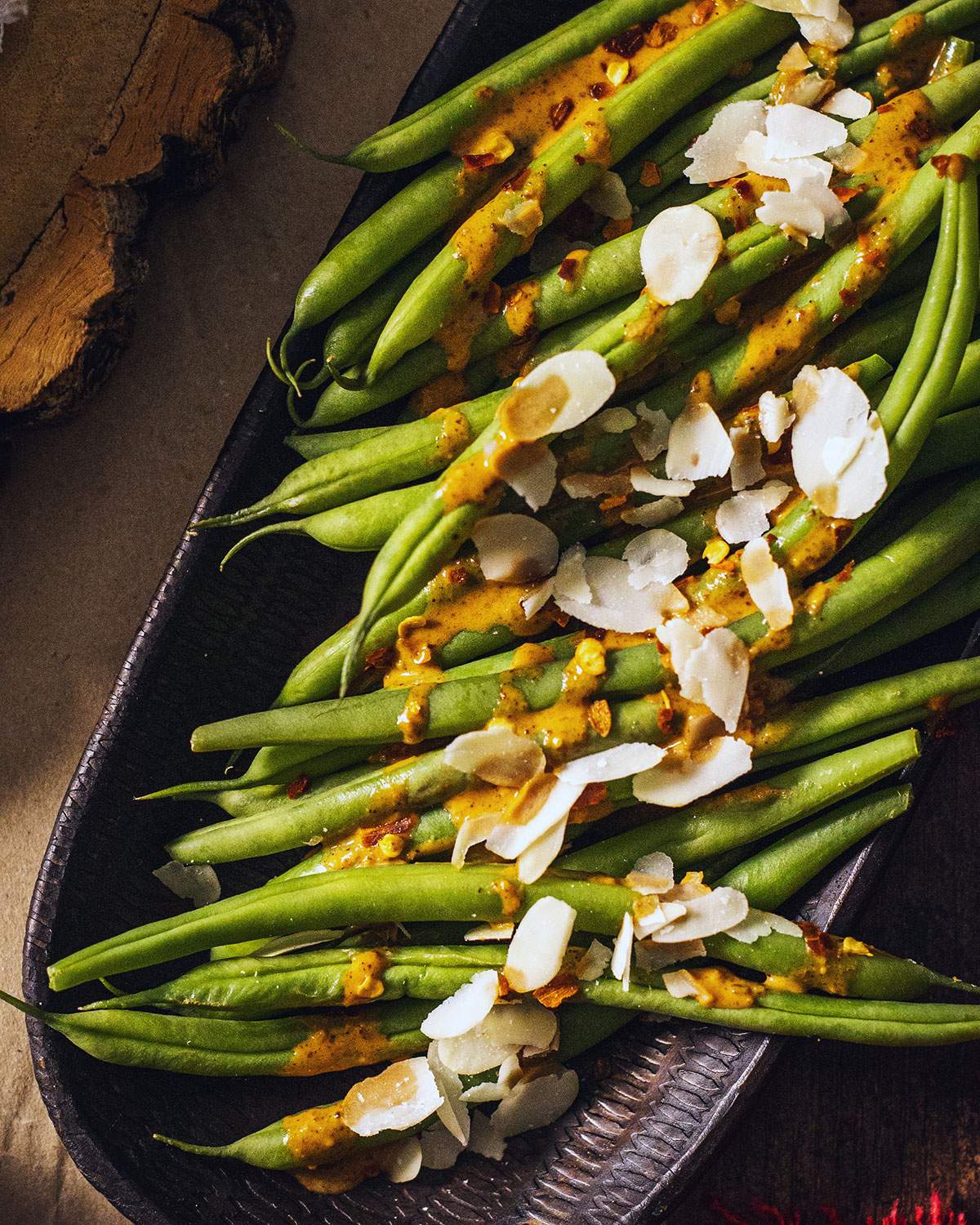 Cooked green beans on a serving platter drizzled with a spicy sauce and almond flakes on top.