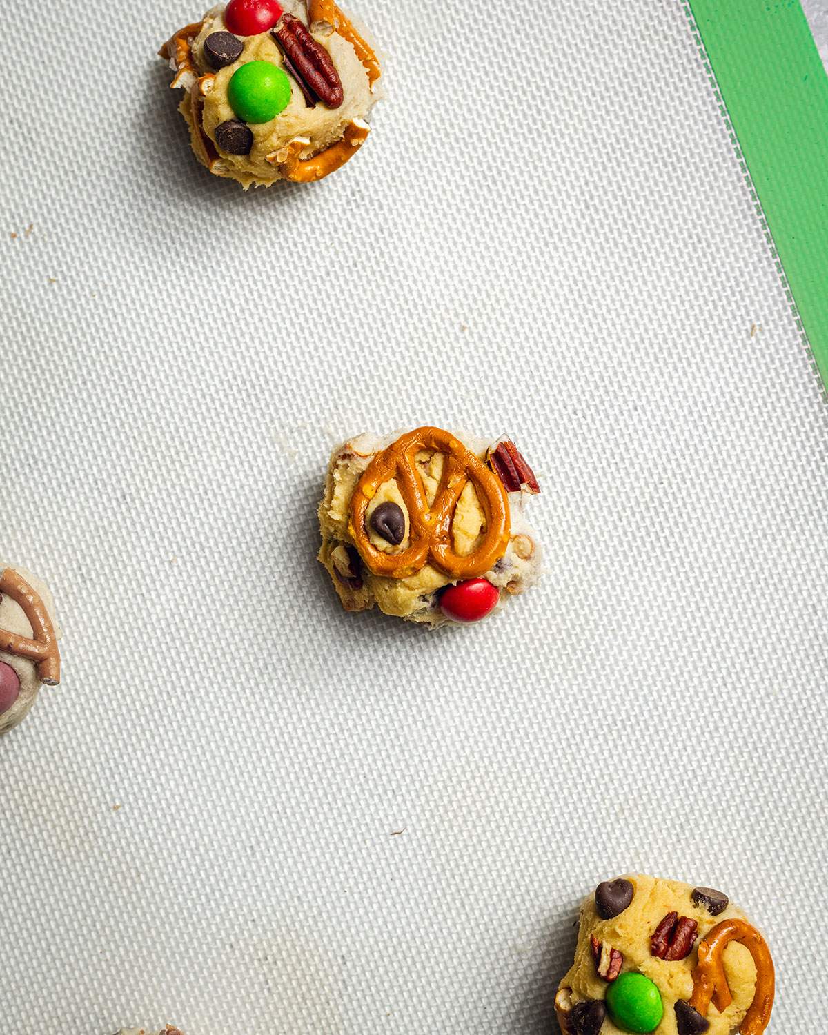 Individual cookie dough balls are seen on a baking mat before baking.