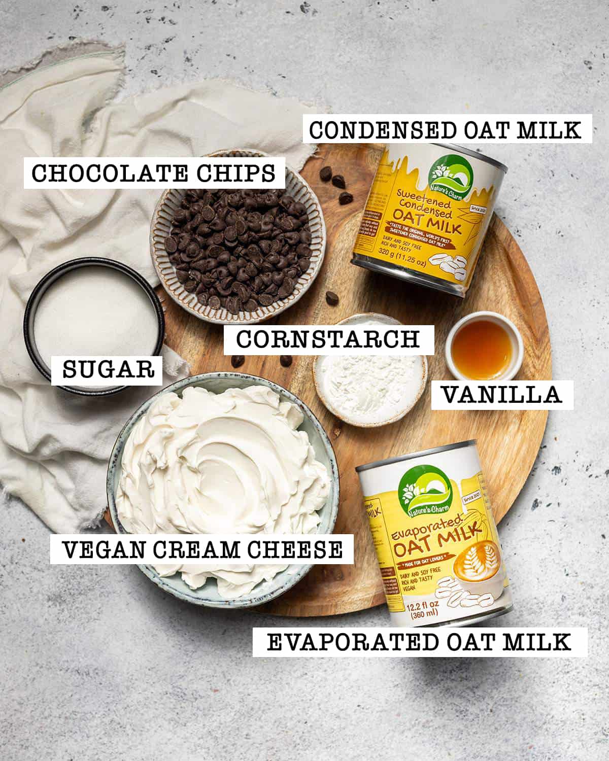 All ingredients for vegan cheesecake filling with chocolate chips on a round tray with labels.