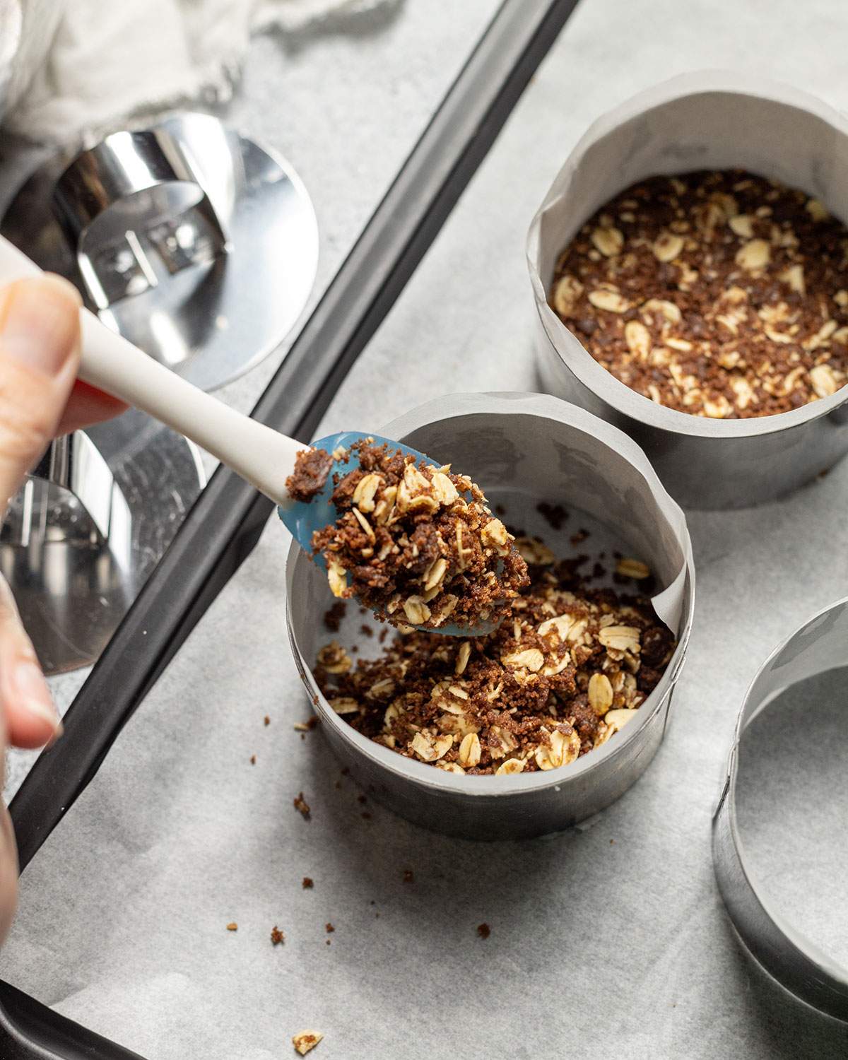 A tiny spatula transferring the biscuit base mix into individual dessert rings.