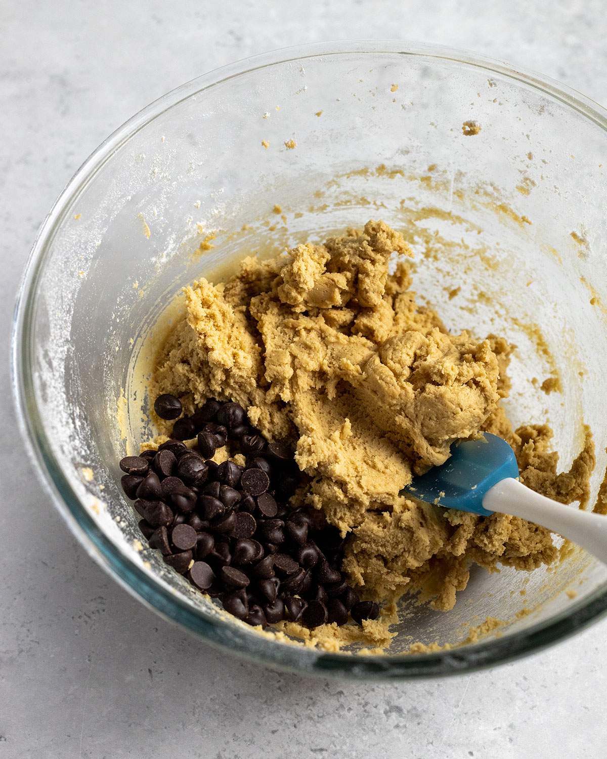 Dark chocolate chips have been added to cookie dough in a mixing bowl.