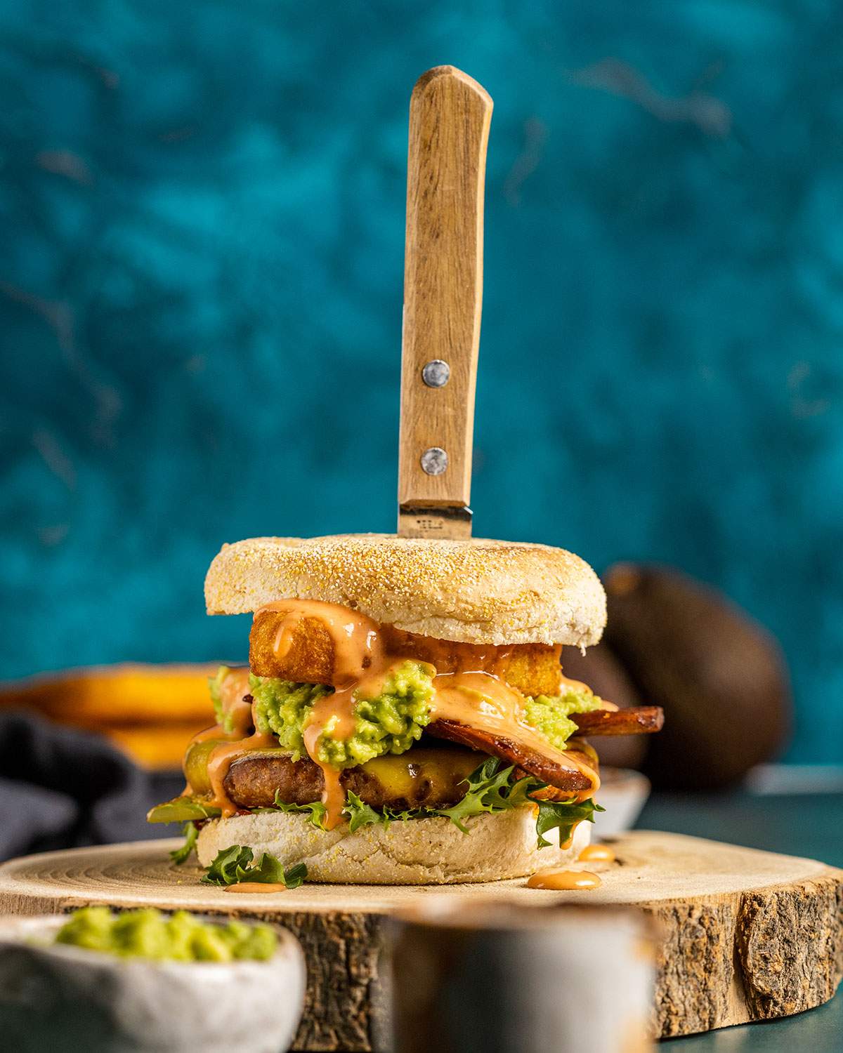 A savory vegan breakfast burger on a wooden serving tray with a knife stuck in the top of the burger.