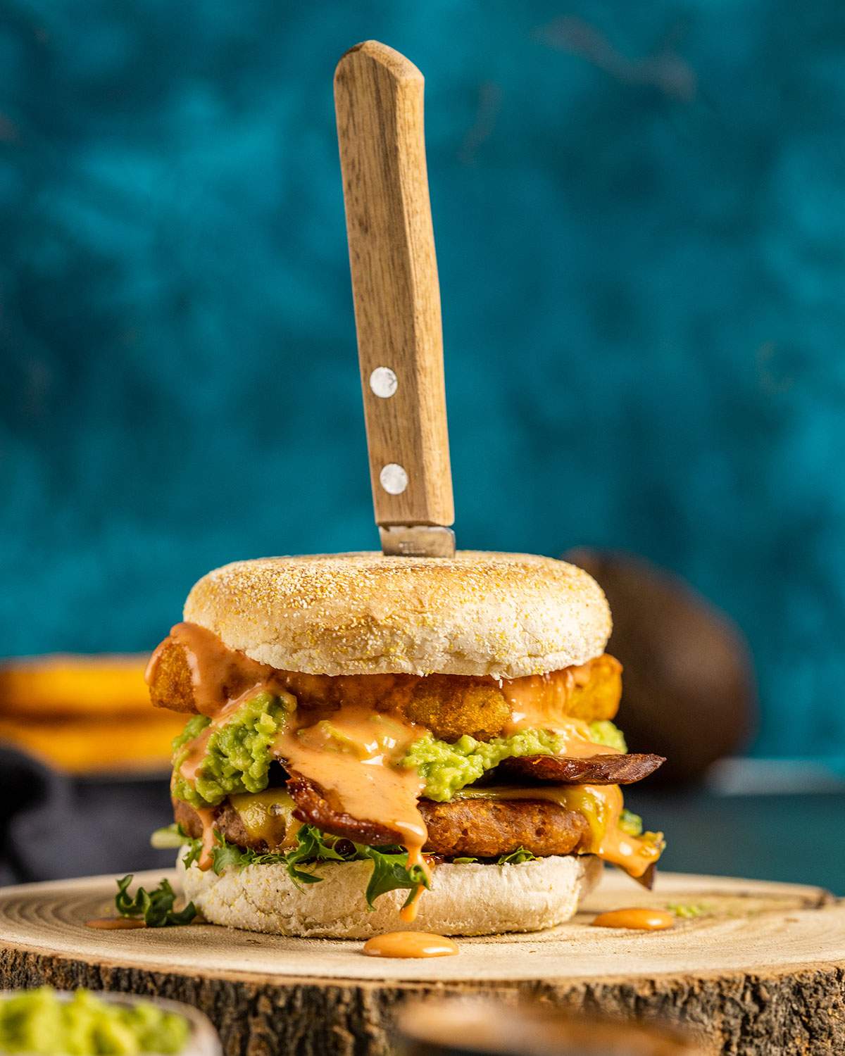 A savory vegan breakfast burger on a wooden serving tray with a knife stuck in the top of the burger.