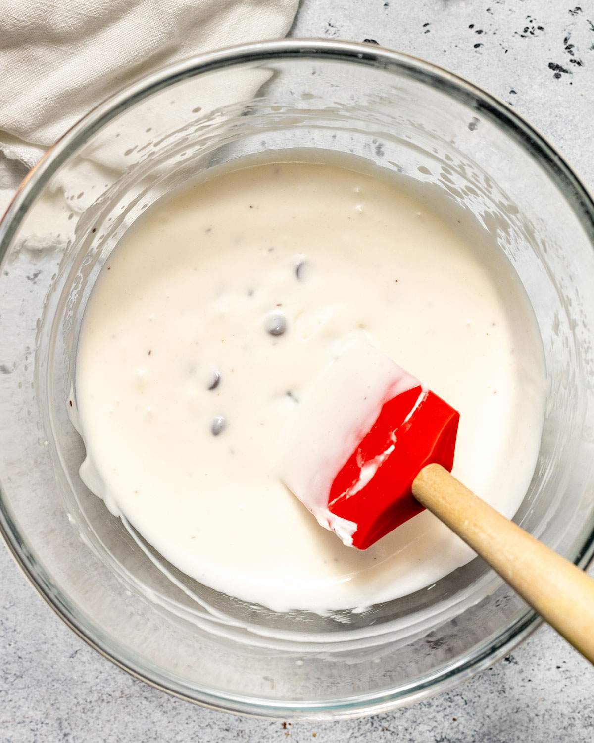 Dark chocolate chips have been folded into the cheesecake mix in a glass bowl with a spatula.