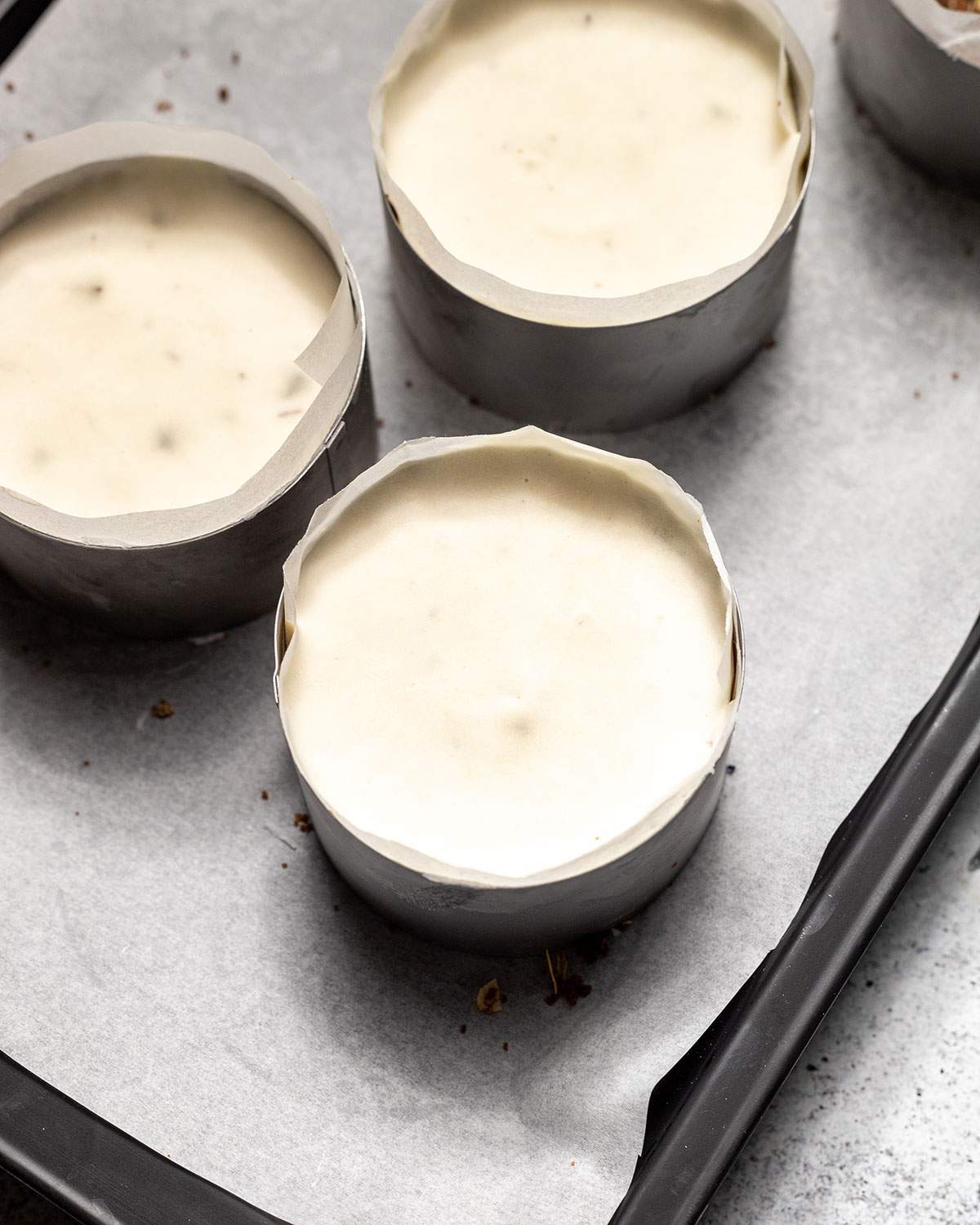 Vegan chocolate chip mini cheesecakes in dessert rings on a lined tray after refrigeration.