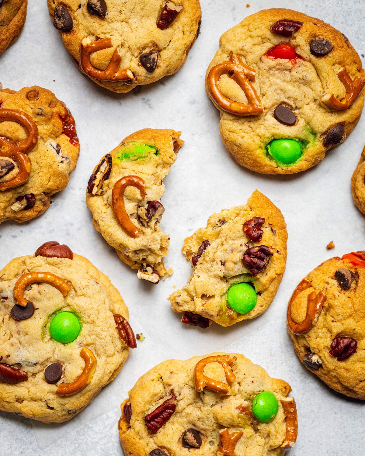 Baked kitchen sink cookies are sitting on white parchment paper with the cookie in the middle broken in two halves.