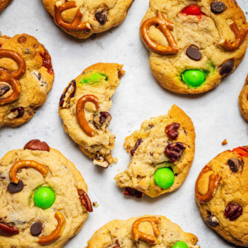 Baked kitchen sink cookies are sitting on white parchment paper with the cookie in the middle broken in two halves.