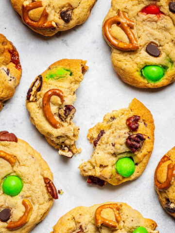 Baked kitchen sink cookies are sitting on white parchment paper with the cookie in the middle broken in two halves.