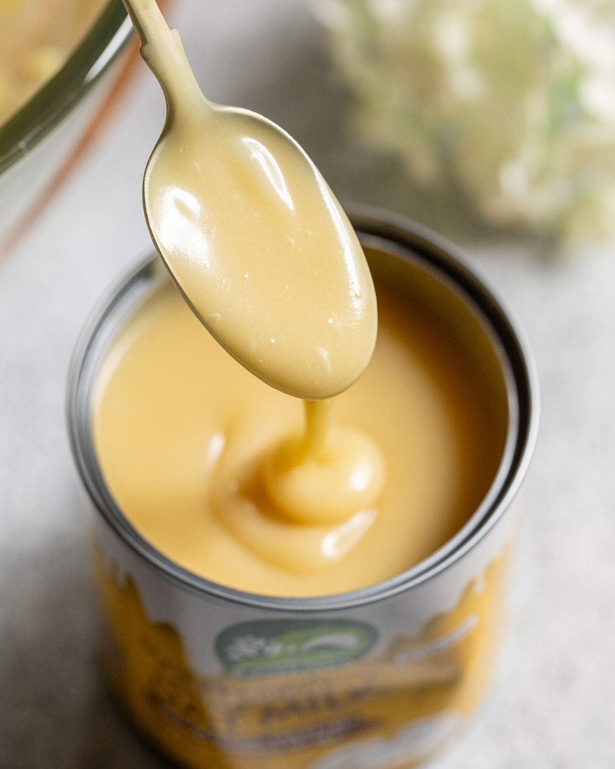 A spoon is lifting condensed oat milk out of a tin.