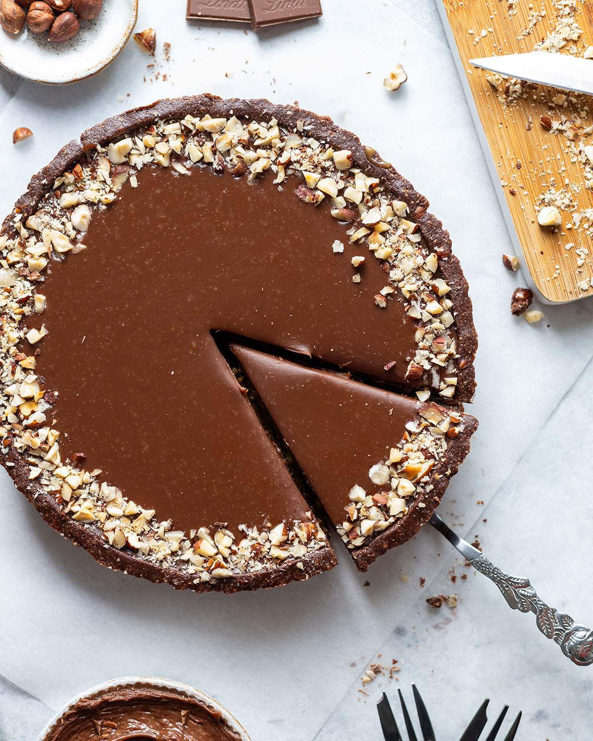 A round vegan chocolate tart seen from above with one slice cut into it.